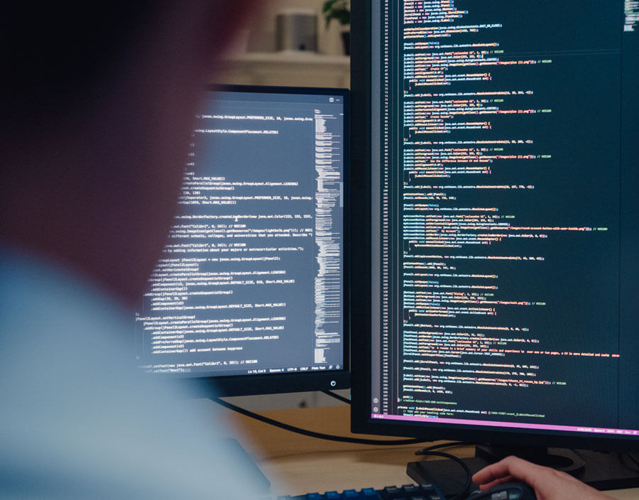 Person looking at code on two monitors.