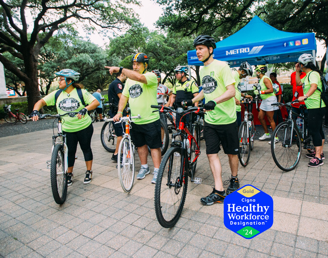 METRO employees gearing up for a wellness bike riding event, showcasing the "Gold Cigna" emblem for Healthy Workforce Designation.