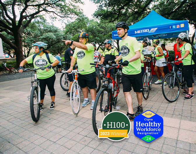 METRO employees gearing up for a wellness bike riding event, showcasing the awarded emblems – the "H100" emblem for being one of the 100 healthiest workplaces in America and the "Gold Cigna" emblem for Healthy Workforce Designation.