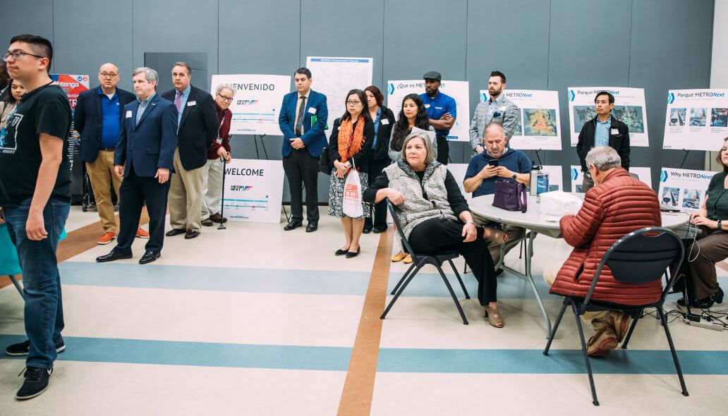 Community members seated and standing with METRONext easel signs in the background.