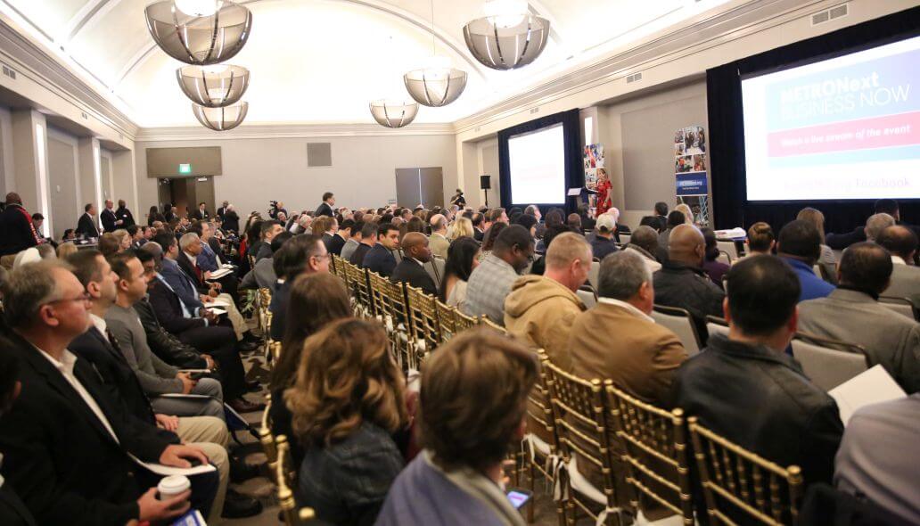 Business representatives seated in hotel ballroom watching presentation by METRO leadership.