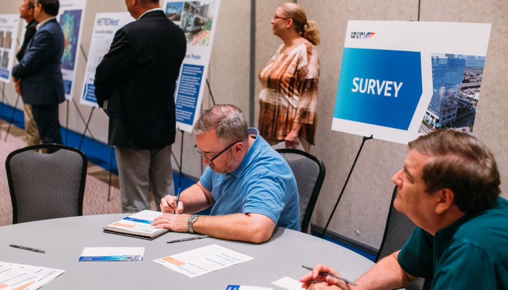 Community member seated at table filling out a survey card during METRONext meeting.