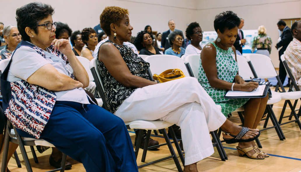 Community members seated at meeting with METRO representatives standing in the background.