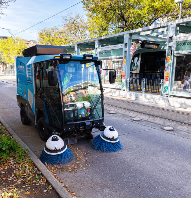 Street sweeper vehicle on the road near a METRORail Red Line platform.