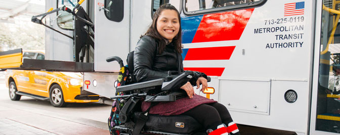 Power wheelchair rider waiting by bus.
