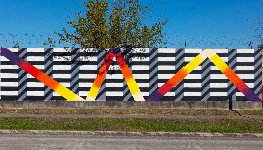 Mural of multicolored zig zag lines against a black and white background along the outer wall of the Kashmere bus operating facility at 5700 Eastex Freeway in Houston