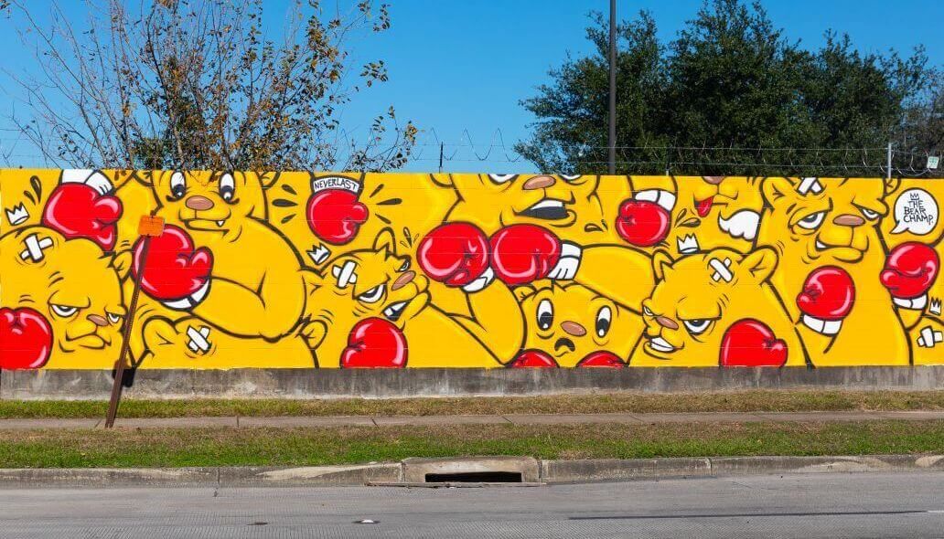 Mural of a series of yellow animated characters wearing boxing gloves along the outer wall of the Kashmere bus operating facility at 5700 Eastex Freeway in Houston