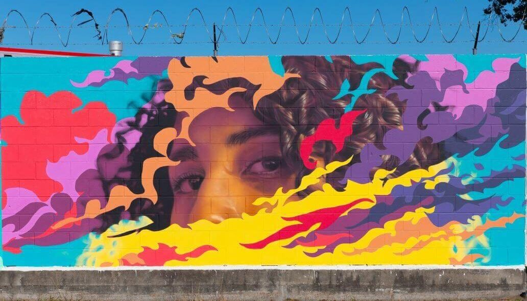 Mural of a female peaking through a series of bright colors along the outer wall of the Kashmere bus operating facility at 5700 Eastex Freeway in Houston