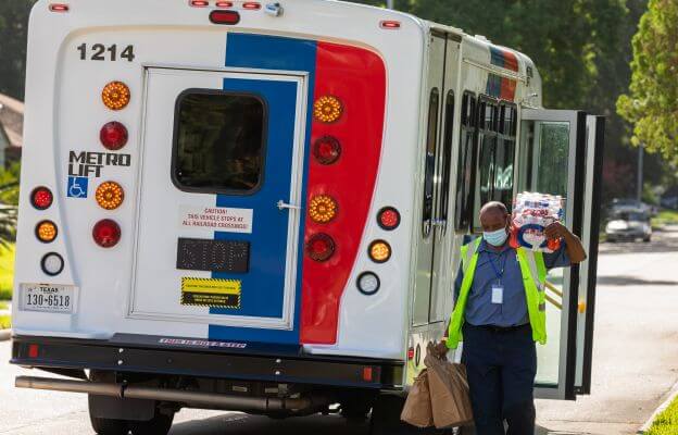 METROLift representative carrying water and a grocery bag alongside a METROLift paratransit van