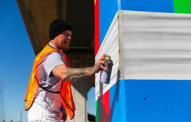 Artist Robin Munro (aka Dread) painting a mural on a column under the elevated METRORail train near Roosevelt Elementary School at 6700 Fulton St. in Houston