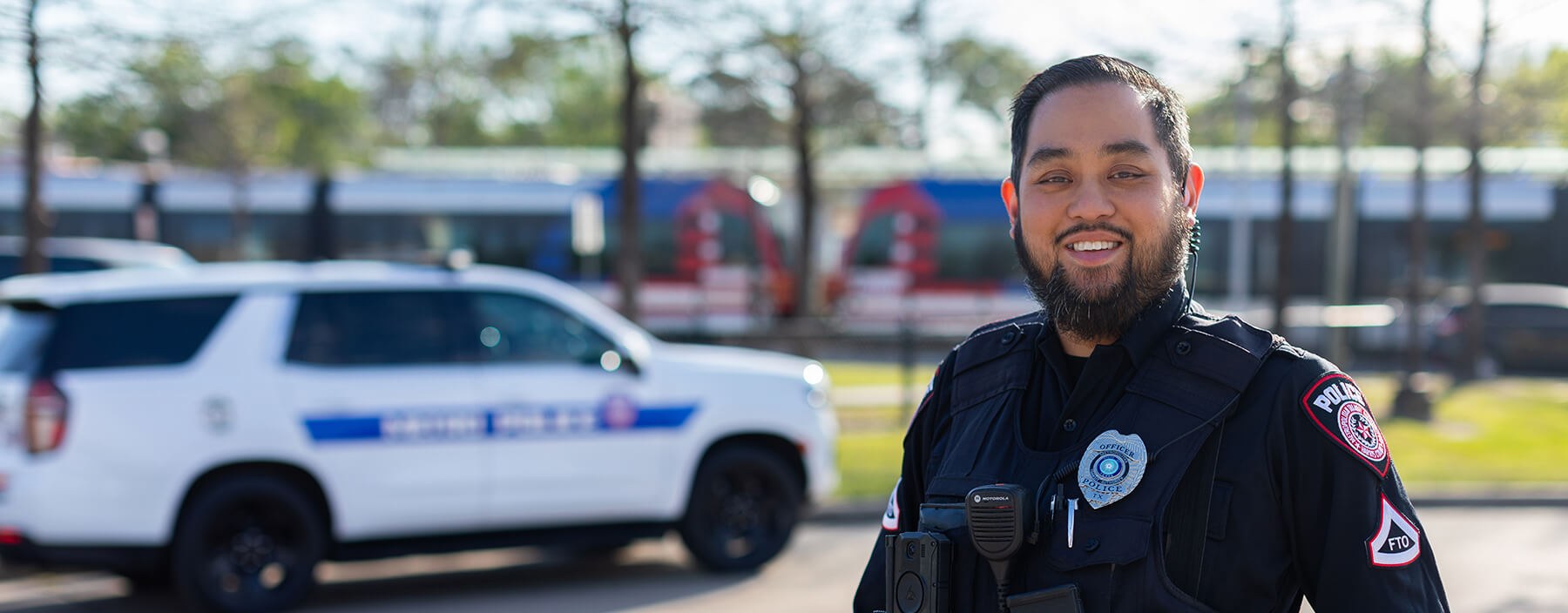 METRO police officer smiling with METRO police car and rail in the background