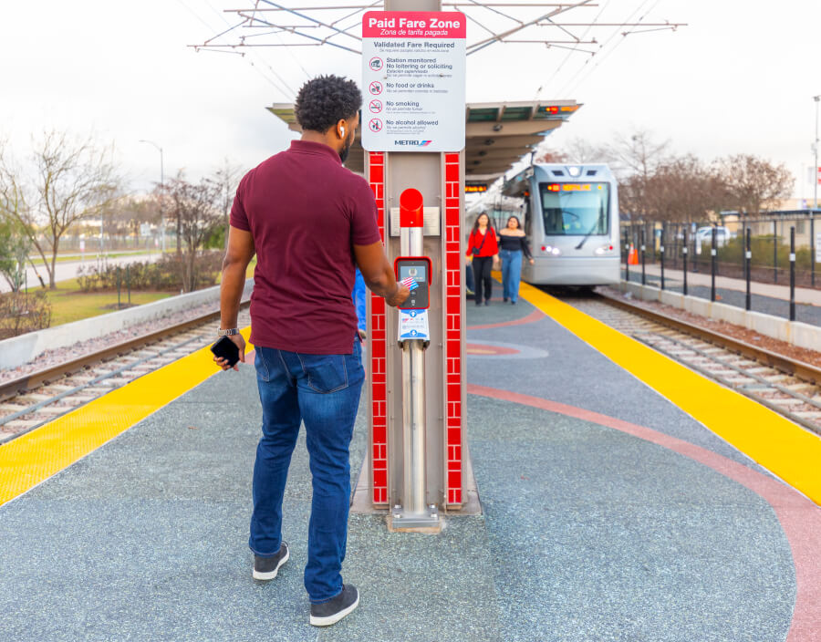 Customer tapping a RideMETRO Fare Card on a METRORail platform fare validator.