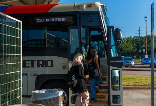 Customers board a METRO commuter express bus at the Kingsland Park & Ride, with cars parked in the background.