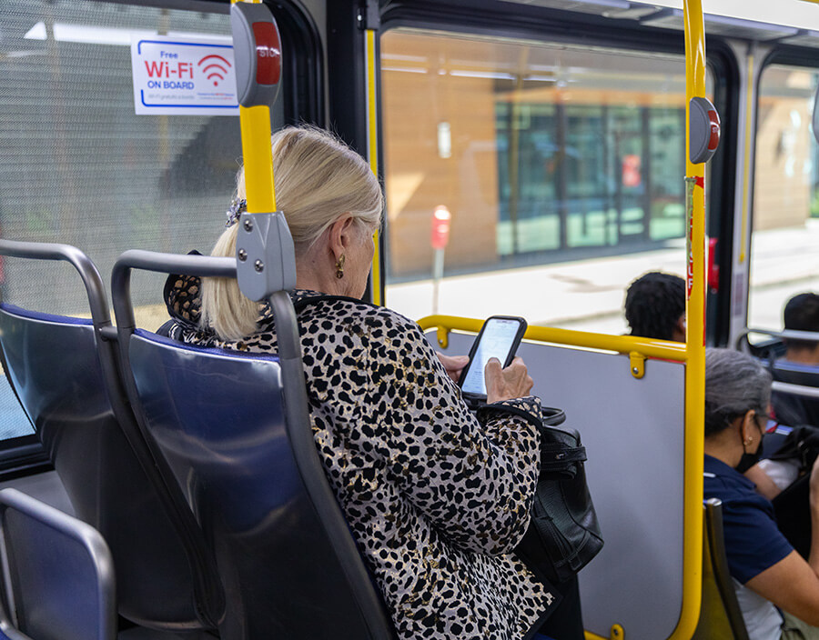 Passenger checking her phone onboard a METRO bus with a free wi-fi sign behind her