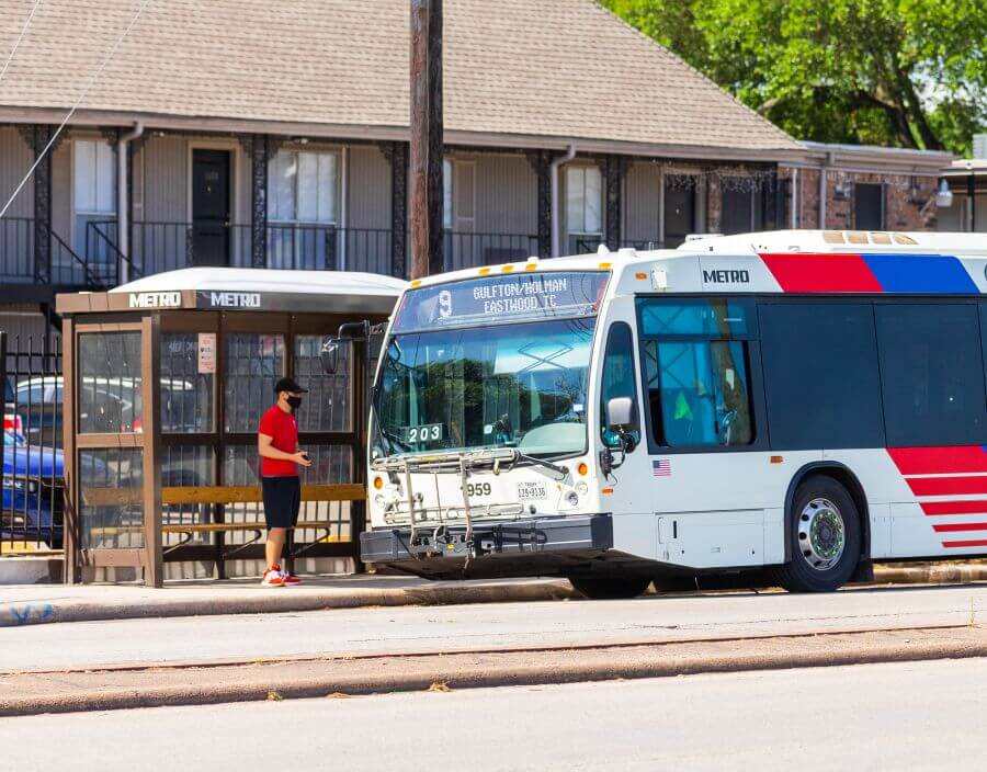 Customer boarding METRO bus at a bus shelter in front of an apartment complex in Gulfton neighborhood.