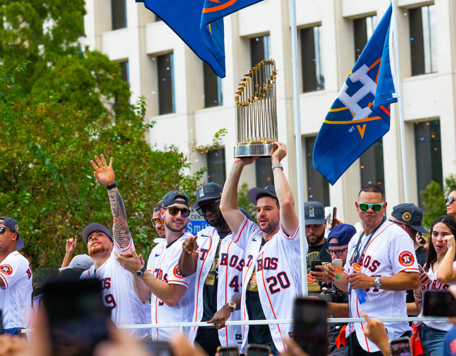 Astros players holding the 2022 World Series trophy while standing on a tour bus in the parade.