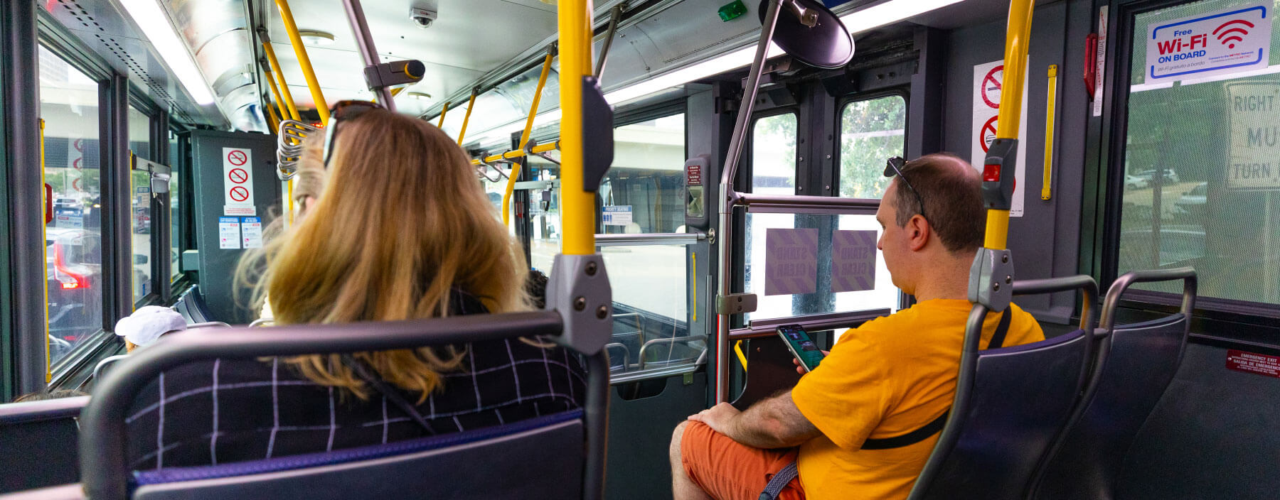 Two riders sitting in the back of METRO local bus, one rider is on a smartphone.