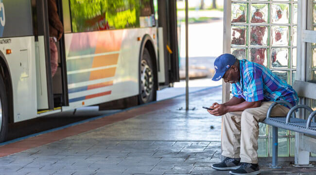 Older man on a mobile phone waiting for his bus at a transit center.