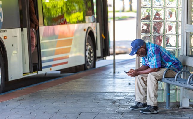 Older man on a mobile phone waiting for his bus at a transit center.
