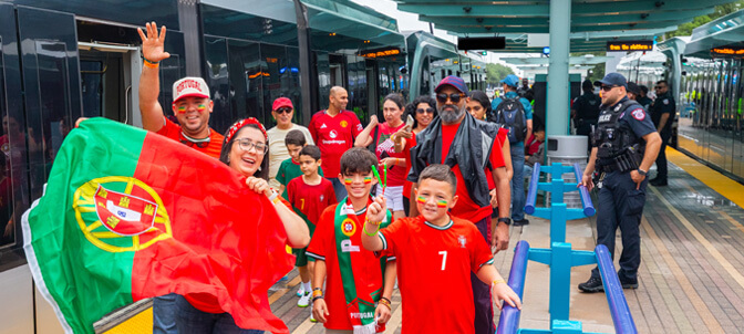 A family waves and holds up Portuguese flag as they walk down the rail platform.