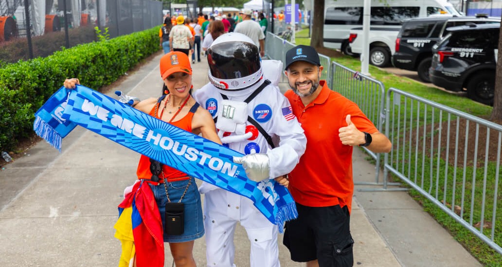 A man and woman posing with the METRO Astronaut mascot and showing their commemorative METRO World Cup scarf.