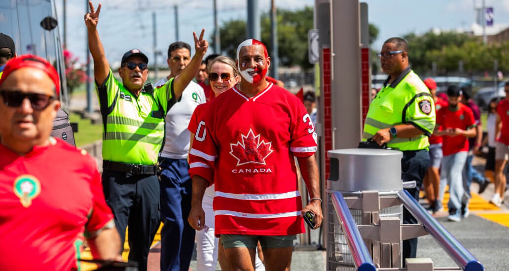 Canada fan wearing red face paint walks down a rail platform.