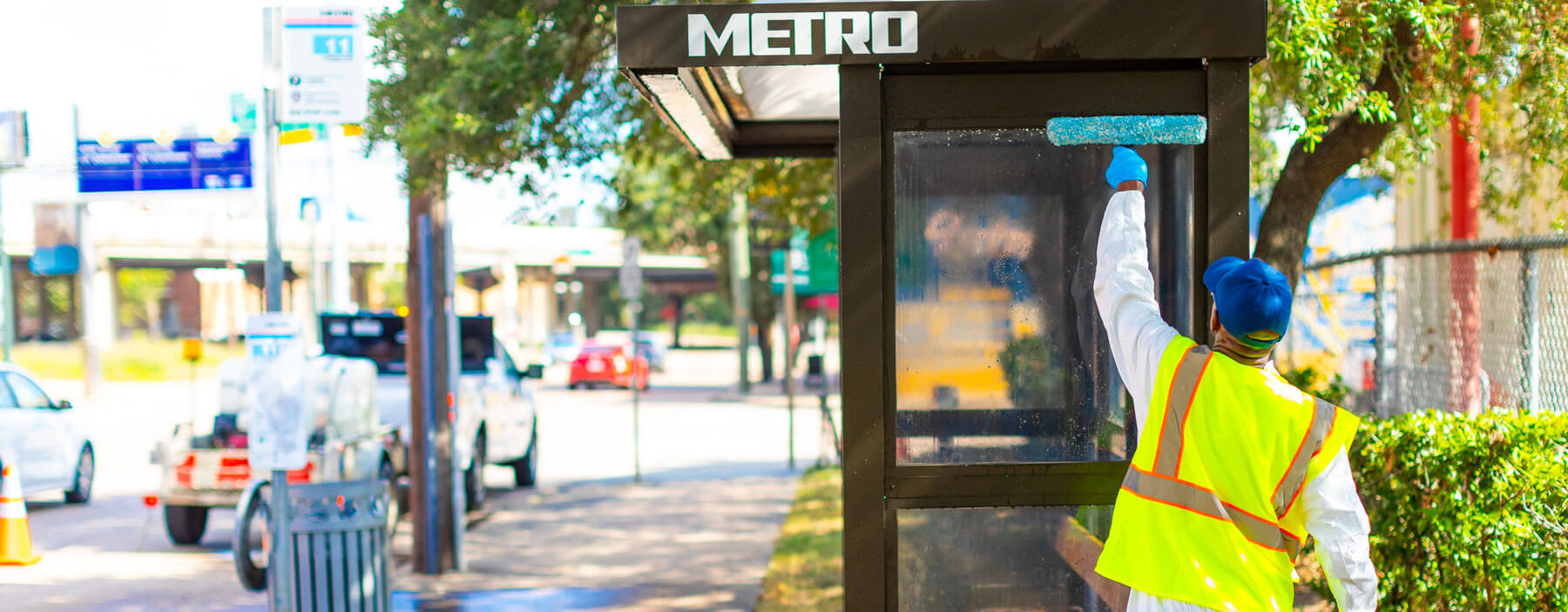 METRO cleaner wiping down bus shelter window with a squeegee.