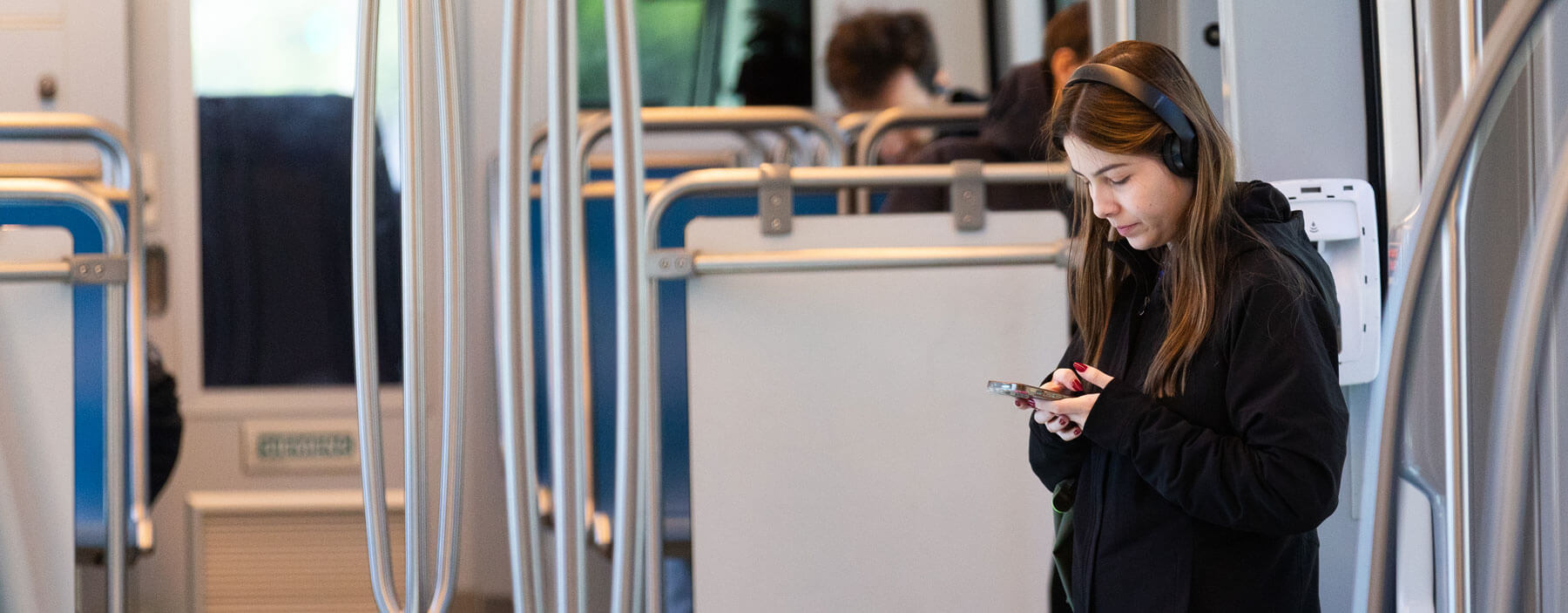 METRORail rider on smartphone with headphones.