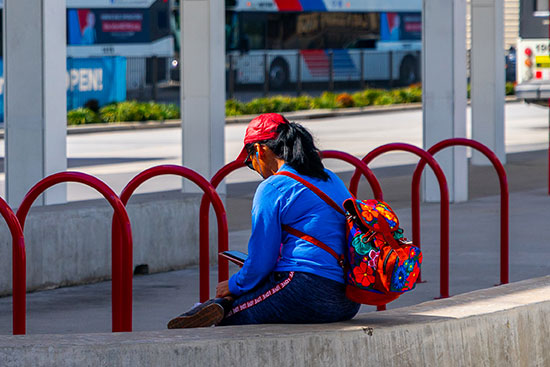 Lady with backpack on smartphone at the Northwest Transit Center while buses are rolling in the background.