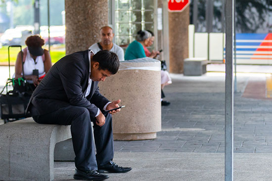 Man sitting down looking at smartphone while waiting on the bus at the Transit Center.