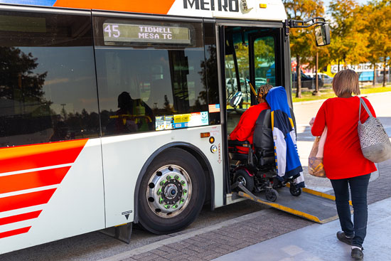 A power wheelchair rider and another rider boarding a local bus at a Transit Center.