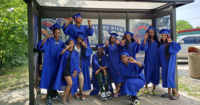 Kashmere seniors celebrate METRO's newest student-designed shelter by taking photos in front of it  in their royal blue raduation gowns.
