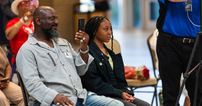 Kashmere freshman and art contest winner, Tianna Newell sits in a chair as local officials priase her efforts. Her father, seated beside her looks on proudly.