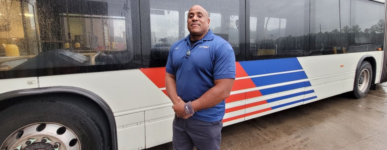 Operator White stands in front of a METRO bus with arms crossed.