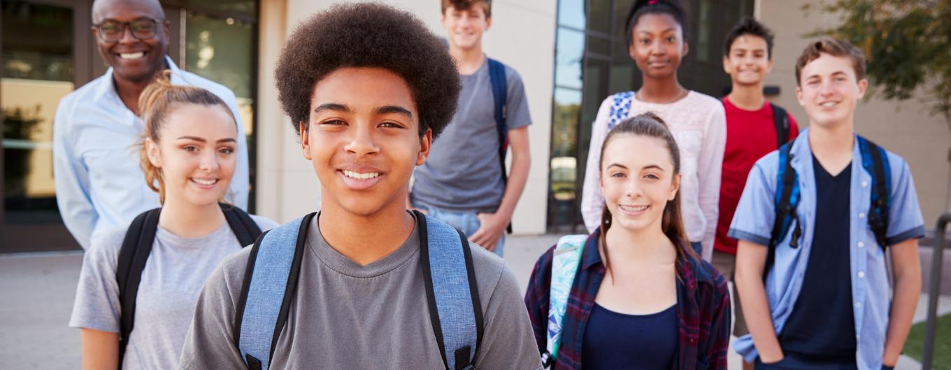 Diverse group of smiling teen students wearing backpacks.