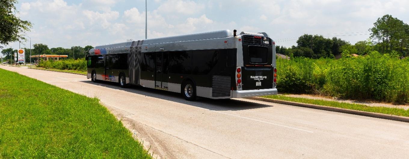 A silver METRO bus drives along a Houston area road.