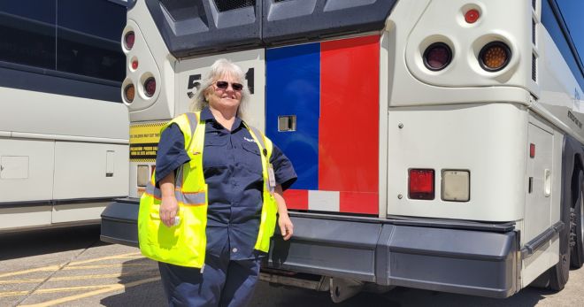 A woman in a yellow safety vest stands near the back of a METRO bus.