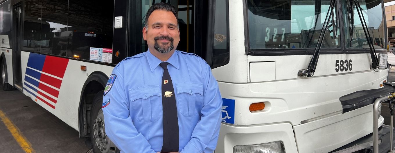 METRO Operator in blue uniform shirt stands in front of his bus.