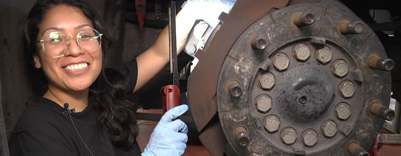 Female mechanic smiling and holding a tool.