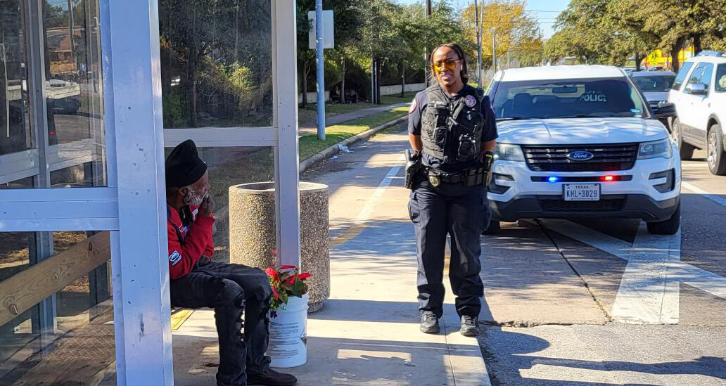 C.A.R.E. Unit uniformed officer with vehicle, talking to person sitting in bus shelter.