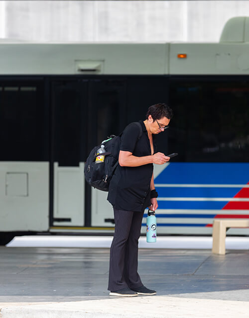 Woman looking down at her cell phone while standing at a bus stop.