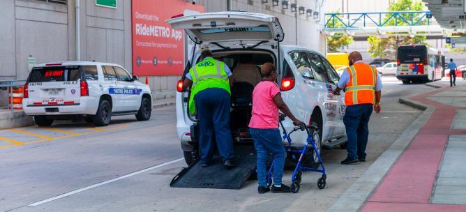 Customer being assisted into METROLIft minivan while another customer walks alongside the vehicle using a walker.