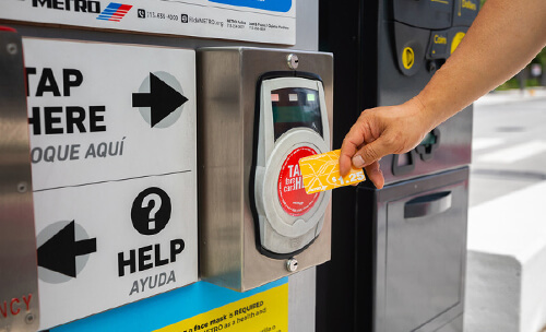 Rider tapping a METRO Money card on a METRORapid Silver Line platform fare validator.